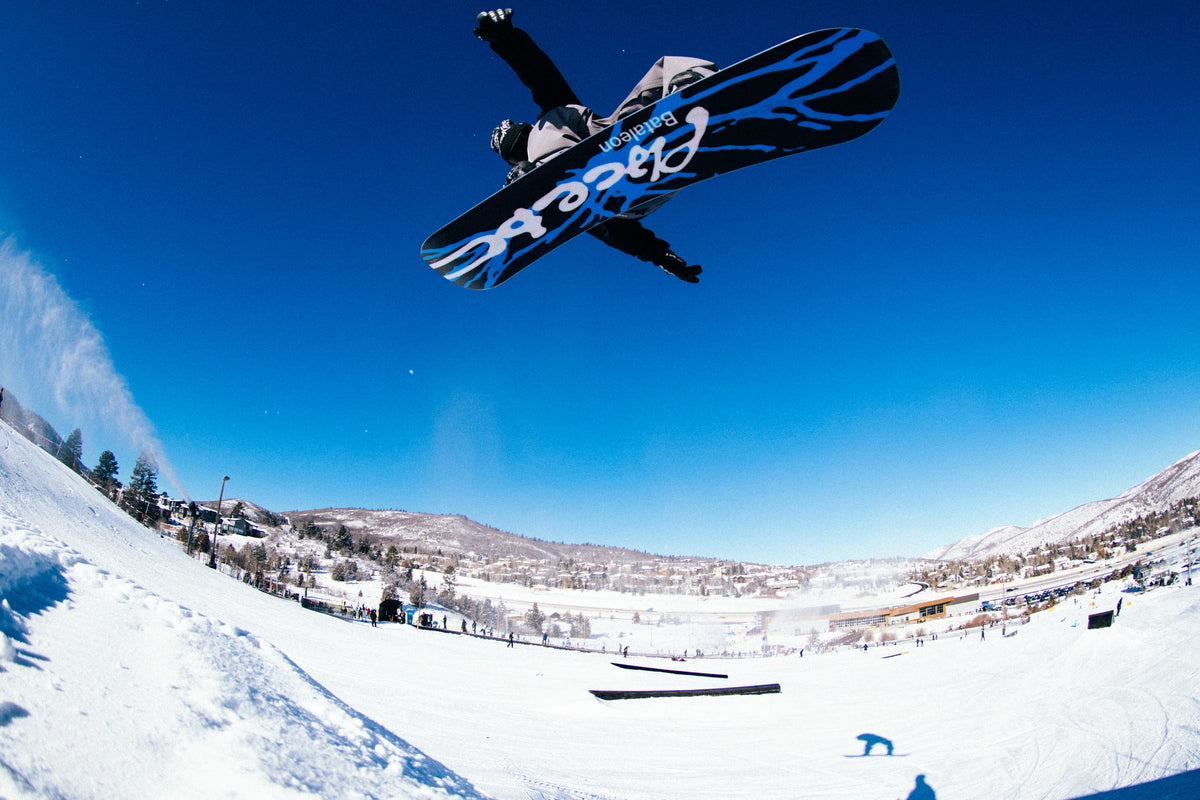 Bataleon Placebo snowboard for men, lifestyle shot showing the snowboard's design and graphics on a snowy background.