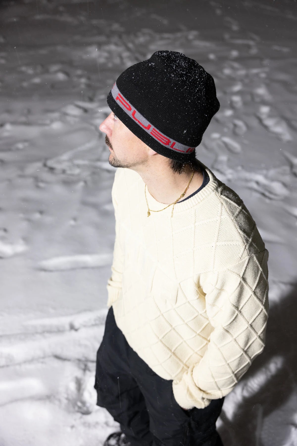 Public Snowboards black and red stretch logo skully beanie, casual winter accessory, shown worn outdoors in a lifestyle setting.