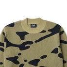 A crewneck knit sweater featuring a bold black abstract camouflage pattern on a khaki-beige base, displayed flat against a solid white background.