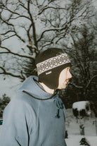 Public Nordic Earflap Beanie in black, a cozy winter accessory with earflaps, worn by a person outdoors.
